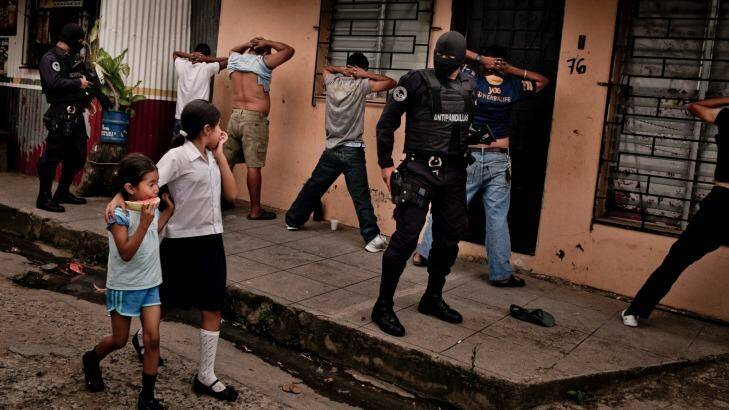 School children walk by as heavily armed members of a police anti-gang force search men in El Salvador. Photo: Tomas Munita 
