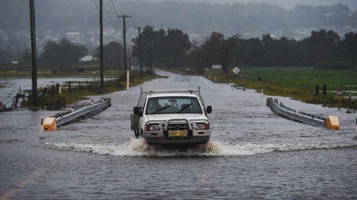 Local farmer crosses the flooded Illawarra Highway at Albion Park after heavy falls across the region. Photo: Nick Moir